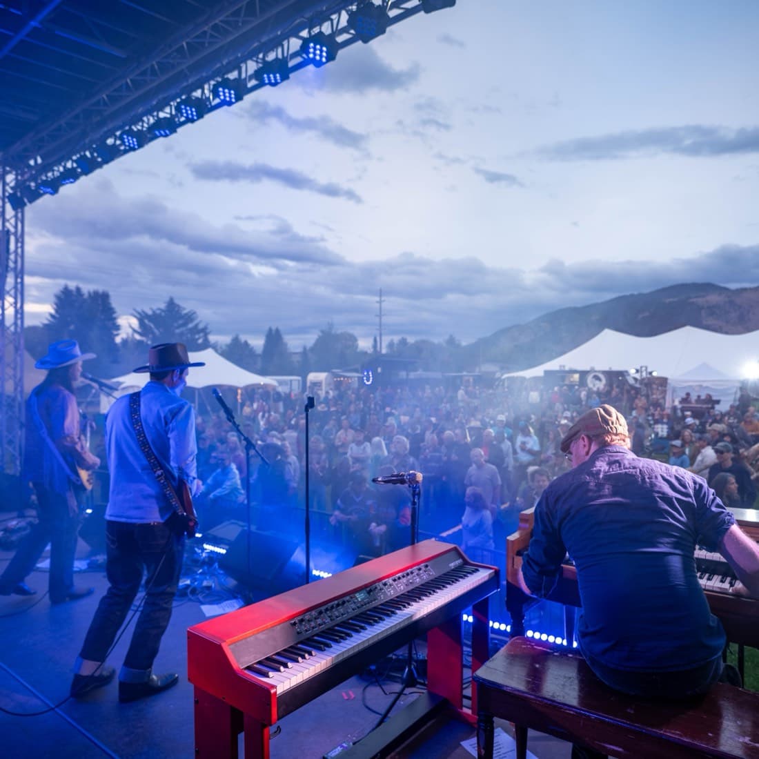 A keyboard player at the front of the stage with the crowd and the valley spread out behind
