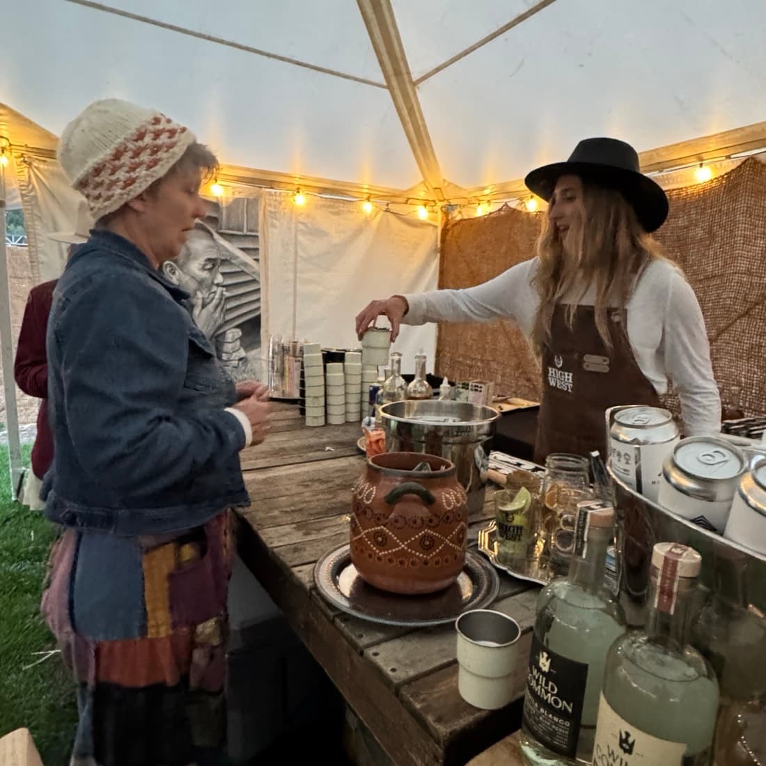 Two makers behind a stall of jars and bottles under strings of light
