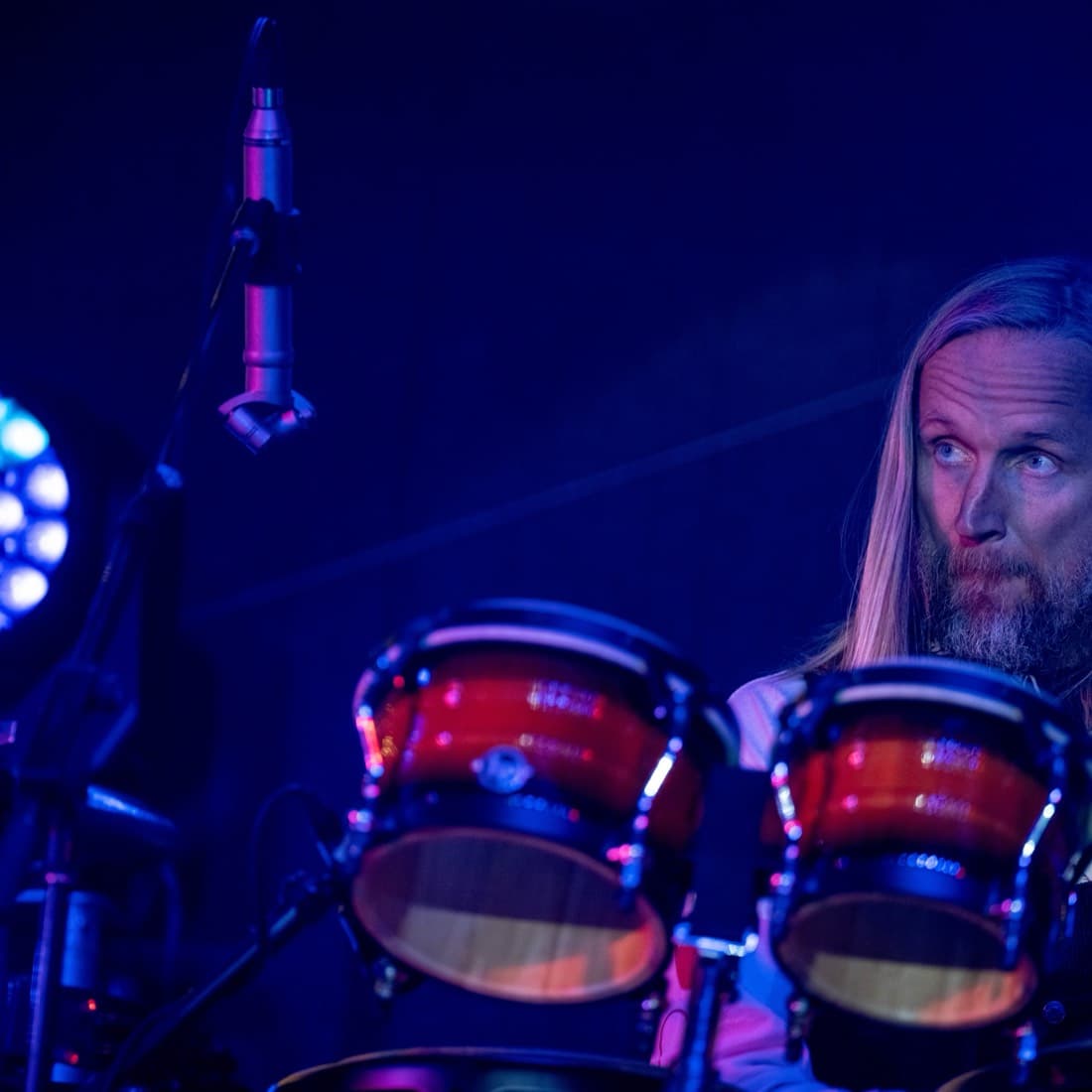 A percussionist behind congas under deep blue stage light