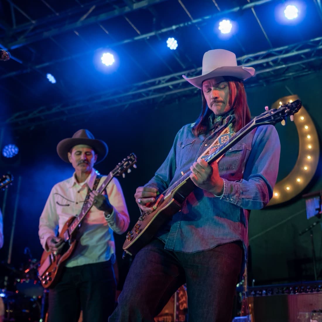 Two musicians playing together at the front of the stage under blue light