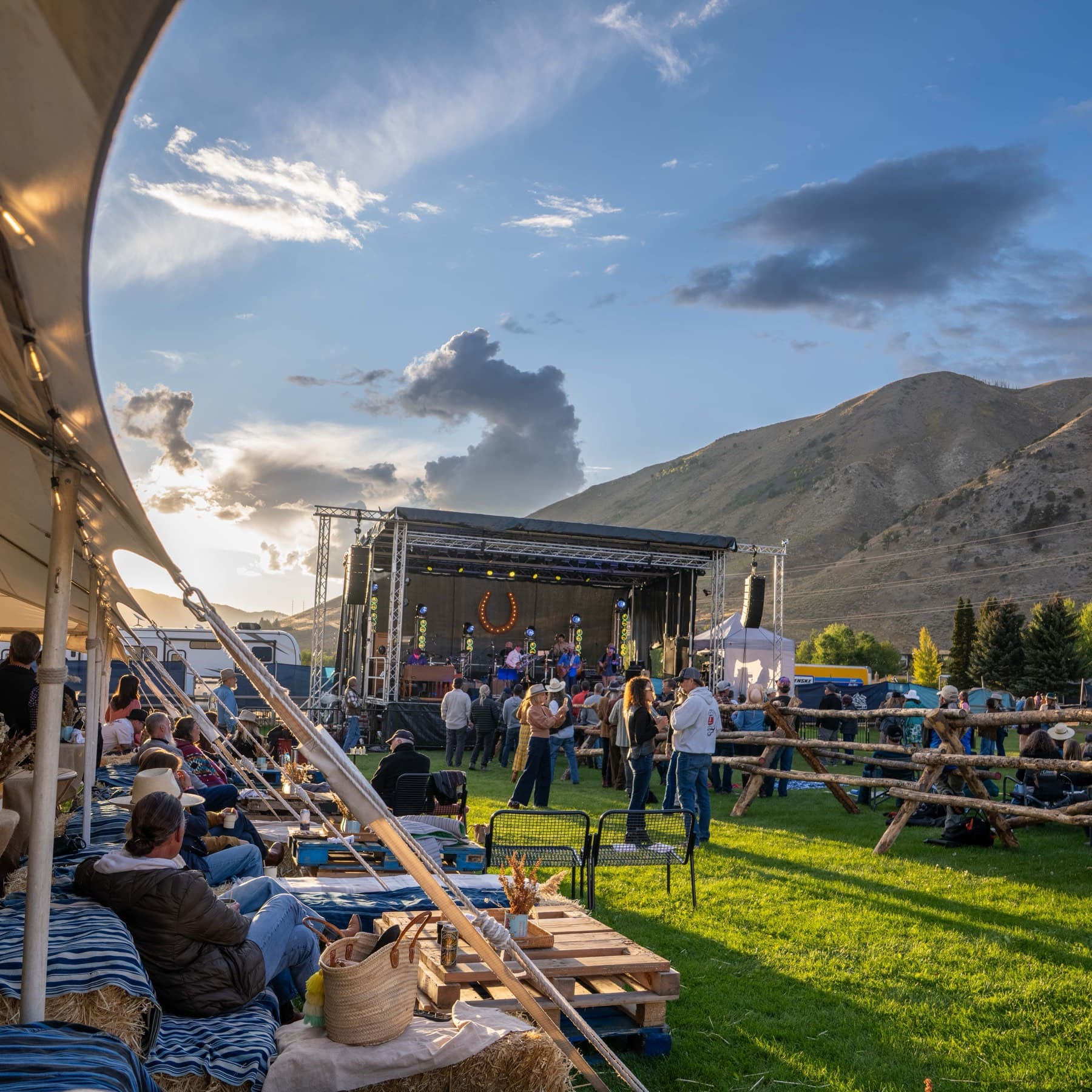 The Horseshoe stage in late afternoon light with the band playing beneath a lit horseshoe, the crowd on the grass in front and a bare ridge rising behind